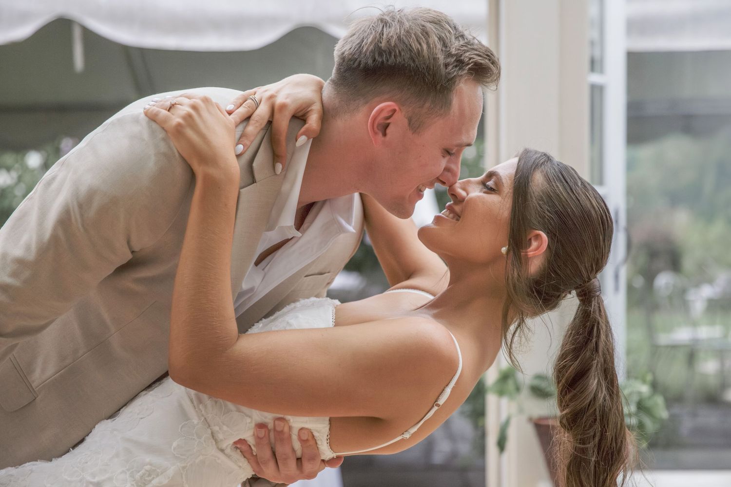 A romantic couple in semi-formal attire share an intimate dance dip pose in a light-filled room.