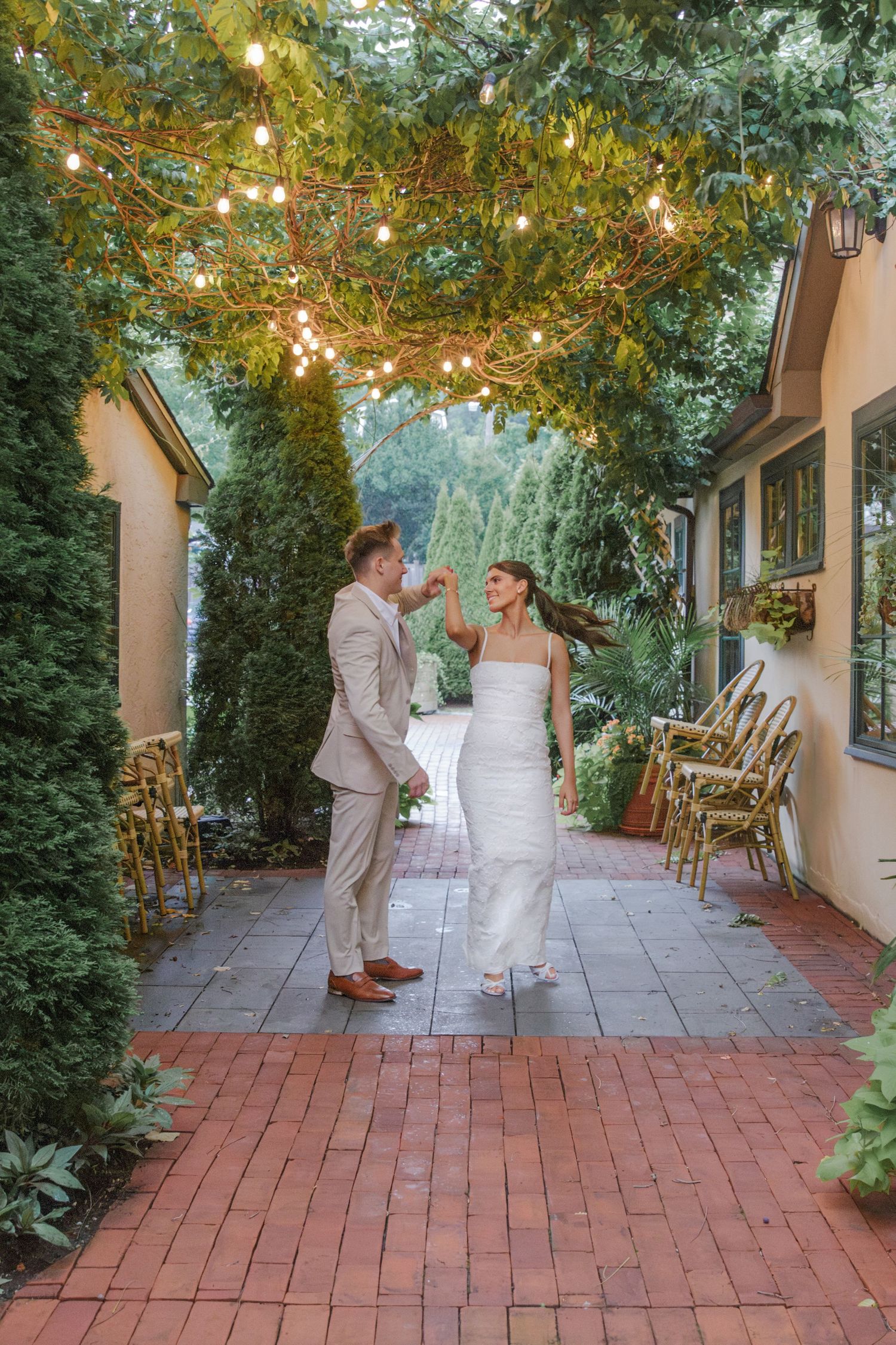 A romantic garden wedding scene with string lights overhead and a brick pathway surrounded by lush greenery.