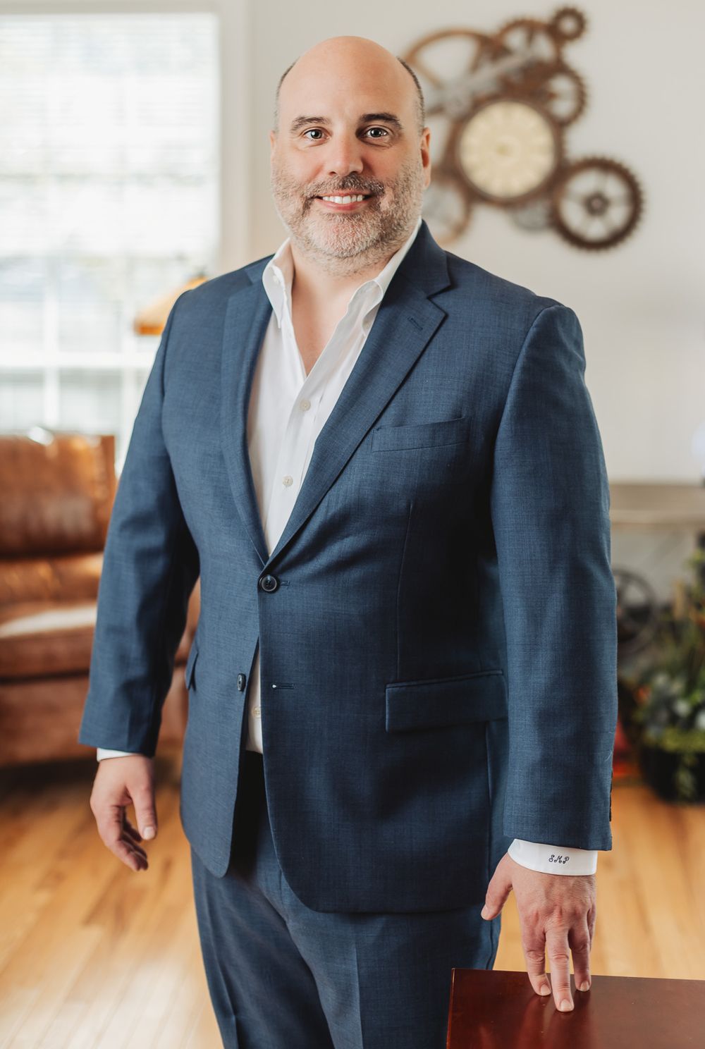 Professional man in blue suit smiling confidently in a well-decorated home office setting.