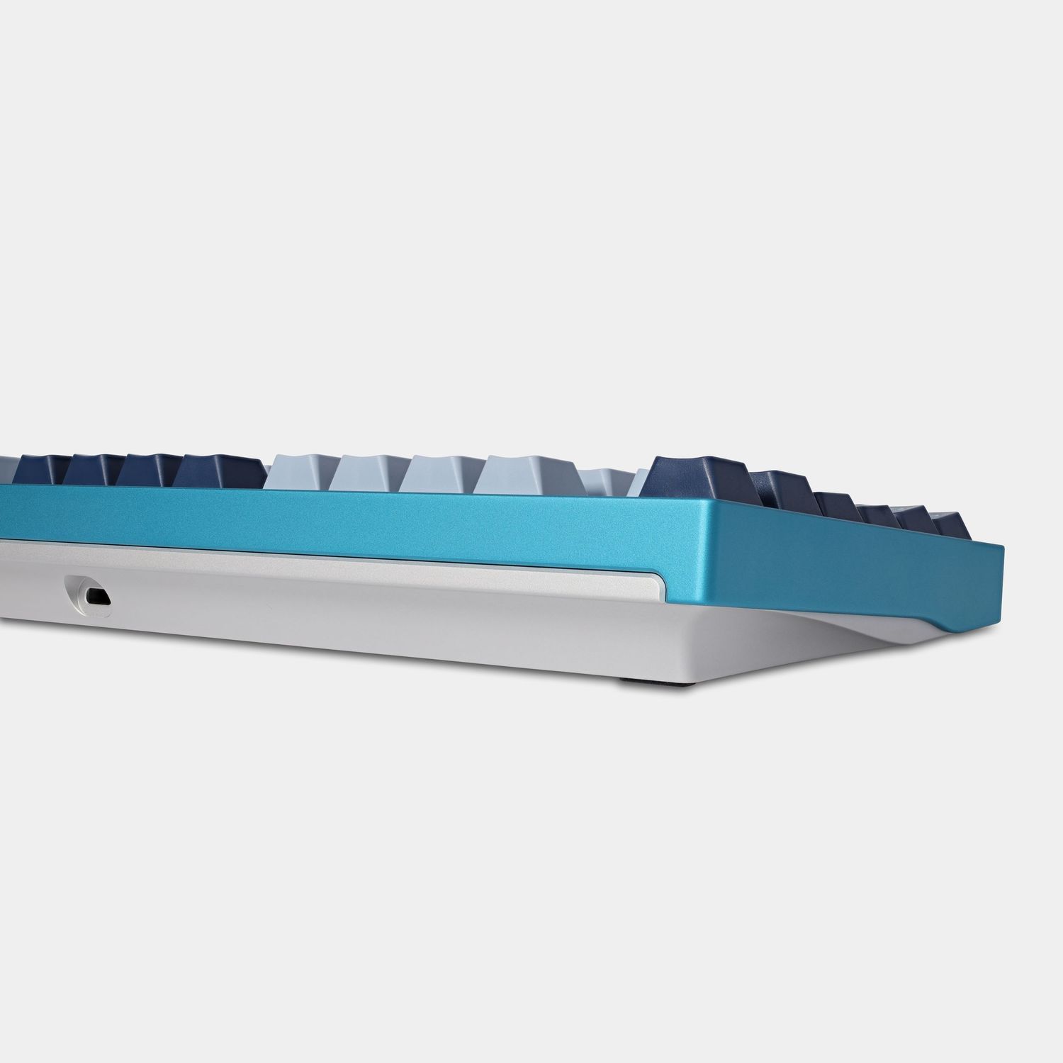 Profile view of a turquoise and silver mechanical keyboard showing angled design.