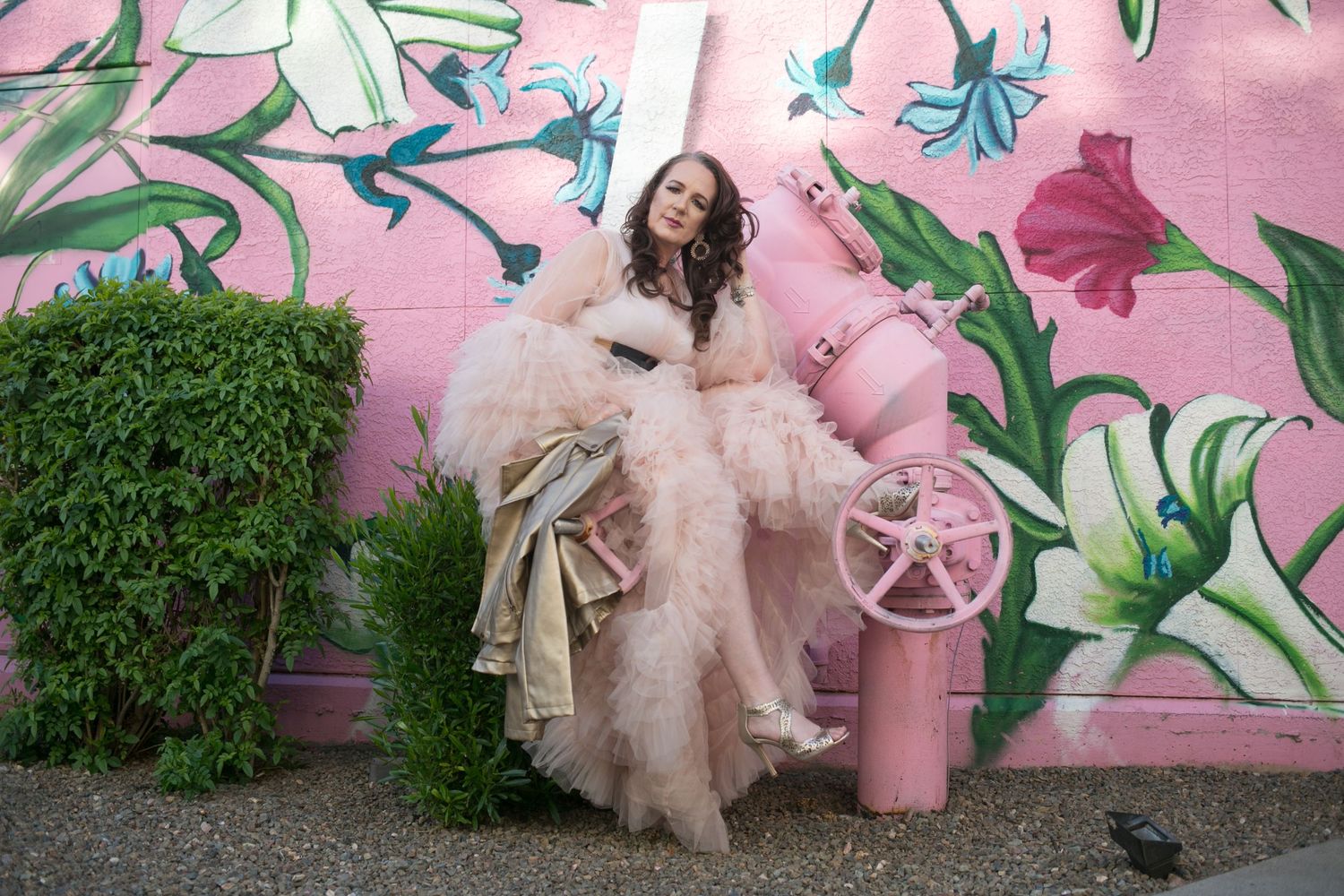 Woman in voluminous pink tulle gown posing by pink fire hydrant with floral mural backdrop.