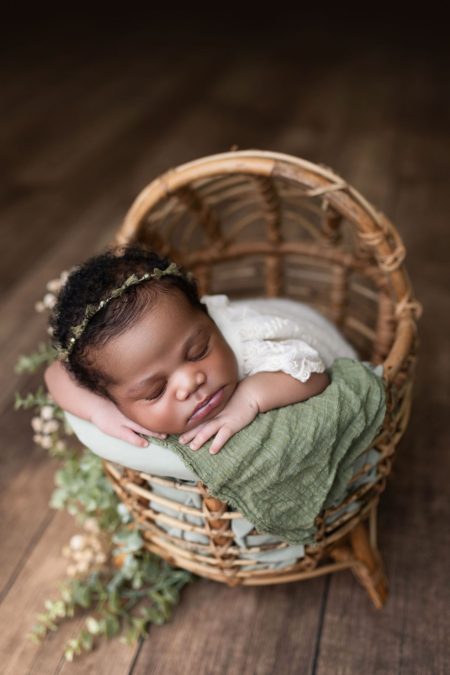 Sleeping newborn baby wrapped in purple swaddle lying on soft white fur with delicate floral headband.