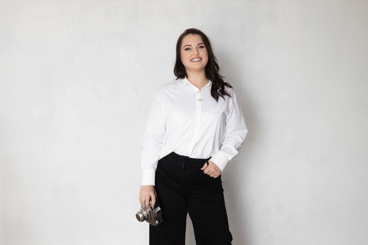 Professional portrait of person in a crisp white button-down shirt and black pants against a light background.