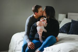 a new mom and dad share an intimate kiss while sitting on their bed