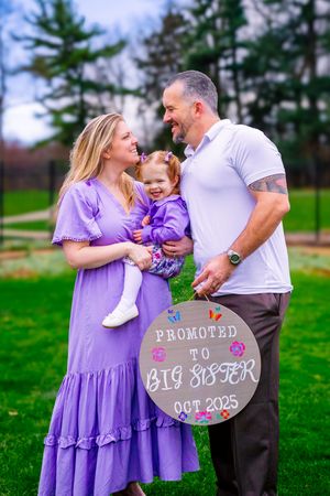 Outdoor maternity session with rich colors and a happy family proudly displaying a sign announcing the pregnancy