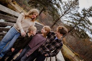 Family of four laughing together on a wooden bridge surrounded by autumn trees and rocky cliffs.