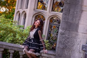 Young woman in black dress posing gracefully by a stone castle wall with stained glass windows and lush greenery.