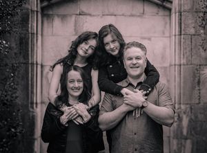 Black and white family portrait of two adults and two teenage girls posing together in front of a stone archway.