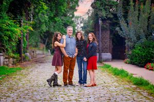 Family of four posing on cobblestone path surrounded by lush greenery during golden hour outdoor portrait.