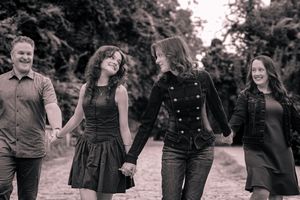 Black and white photo of a happy family of four holding hands and walking together outdoors on a scenic path.