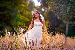 Young woman in white dress standing among wildflowers in a lush garden, smiling warmly in golden hour light.