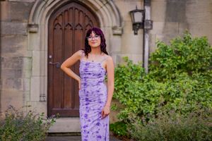 Woman in purple tie-dye maxi dress posing before gothic stone church doorway with lush greenery.