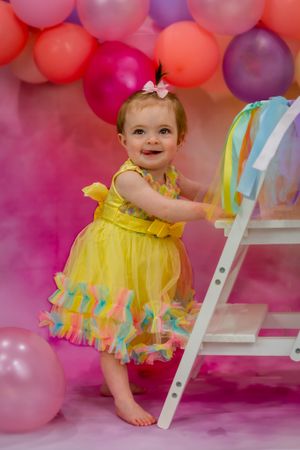 adorable first birthday photoshoot featuring a sweet girl in a. yellow dress with background and bubbles