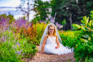 Girl celebrates first holy communion posed outdoors in a garden of flowers