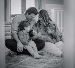 a family snuggles their new baby sitting on the floor in the nursery