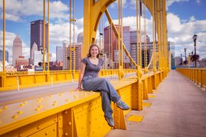 A woman sits on the yellow railing of Pittsburgh's Roberto Clemente Bridge with the city skyline behind her.
