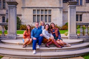 Family poses naturally outdoors with happy smiles and sunlight highlighting their faces