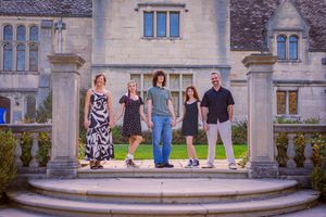 Five people posing on stone steps outside a grand historic mansion with lush green gardens.