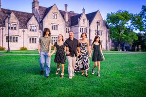 Family of five walking on lush green lawn in front of elegant stone manor house at dusk.