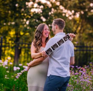 Expecting couple standing in tall grass at sunset with warm colors and a beautiful, calm expression as they display the sonogram pictures