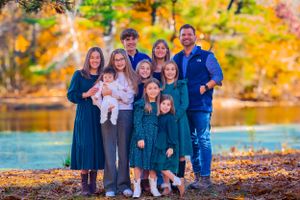 Family poses naturally outdoors with happy smiles and sunlight highlighting their faces
