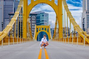 Man crouching on yellow bridge with city skyline and blue sky in Pittsburgh, Pennsylvania.