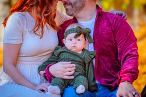 Family poses naturally outdoors with happy smiles and sunlight highlighting their faces