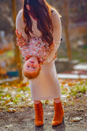 Mother playing with daughter outdoors candidly smiling, dressed in stylish attire, with soft golden sunlight highlighting their