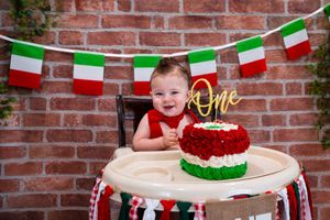 Baby's first birthday cake smash with Italian flag bunting, red and green cake, and a golden 'One' topper.