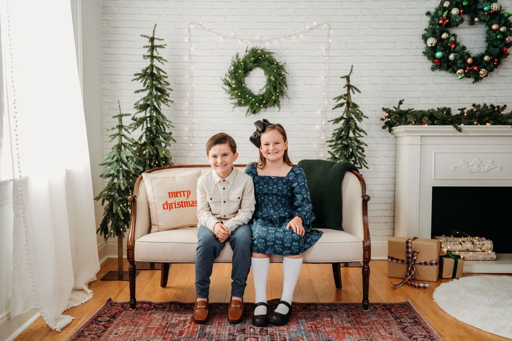 A festive holiday living room with a white couch, Christmas trees, wreaths, and holiday decor by the fireplace.