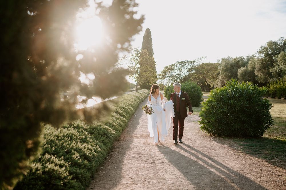 Silhouettes of people walking along a sunlit garden path with dramatic lens flare and lush greenery.