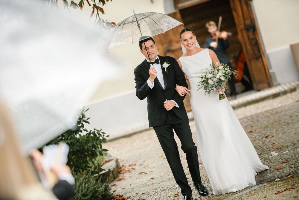 A bride and groom share a romantic moment in their wedding attire against a rustic stone wall background.