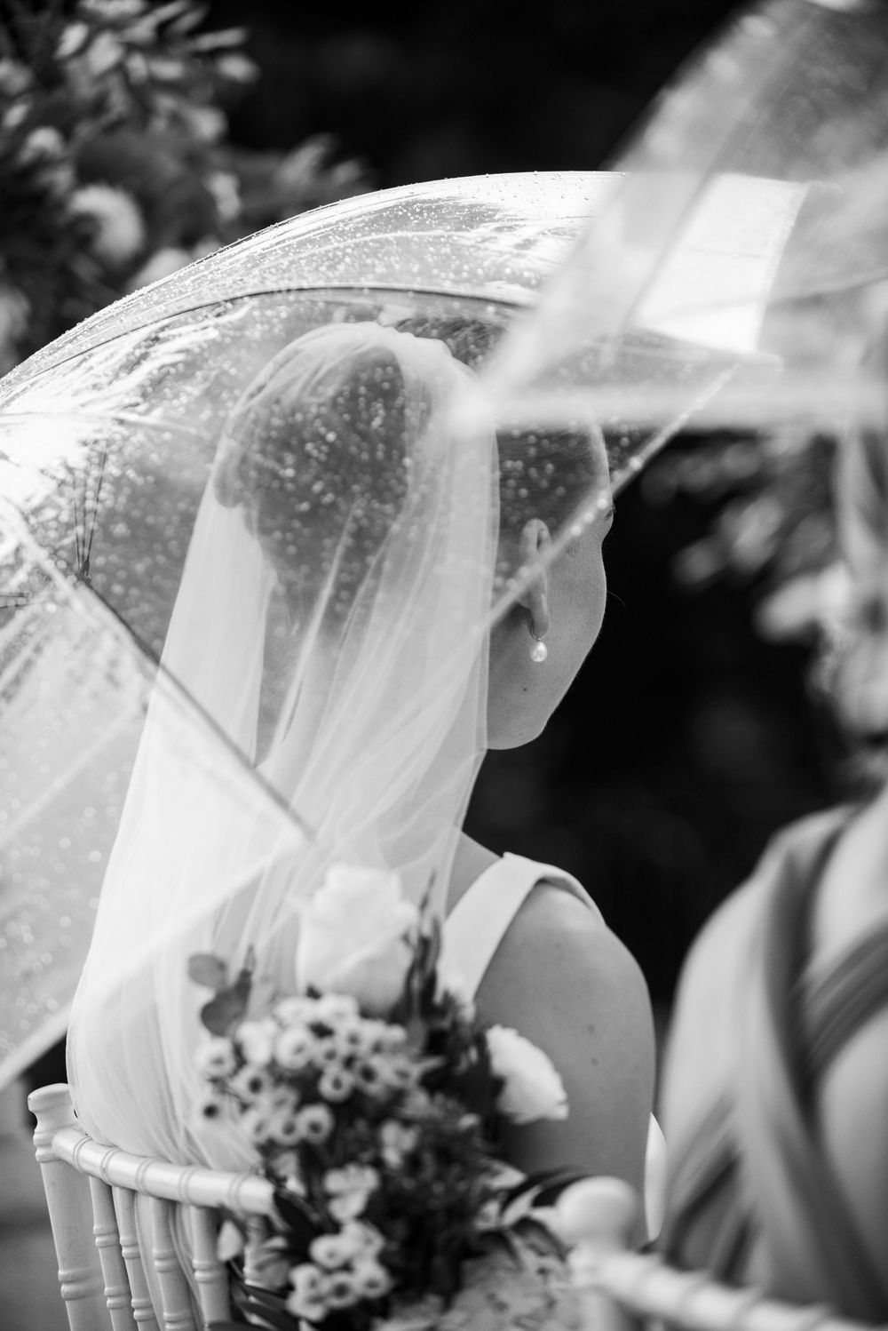 A row of bridesmaids wearing white veils stand together holding bouquets in this black and white wedding photograph.
