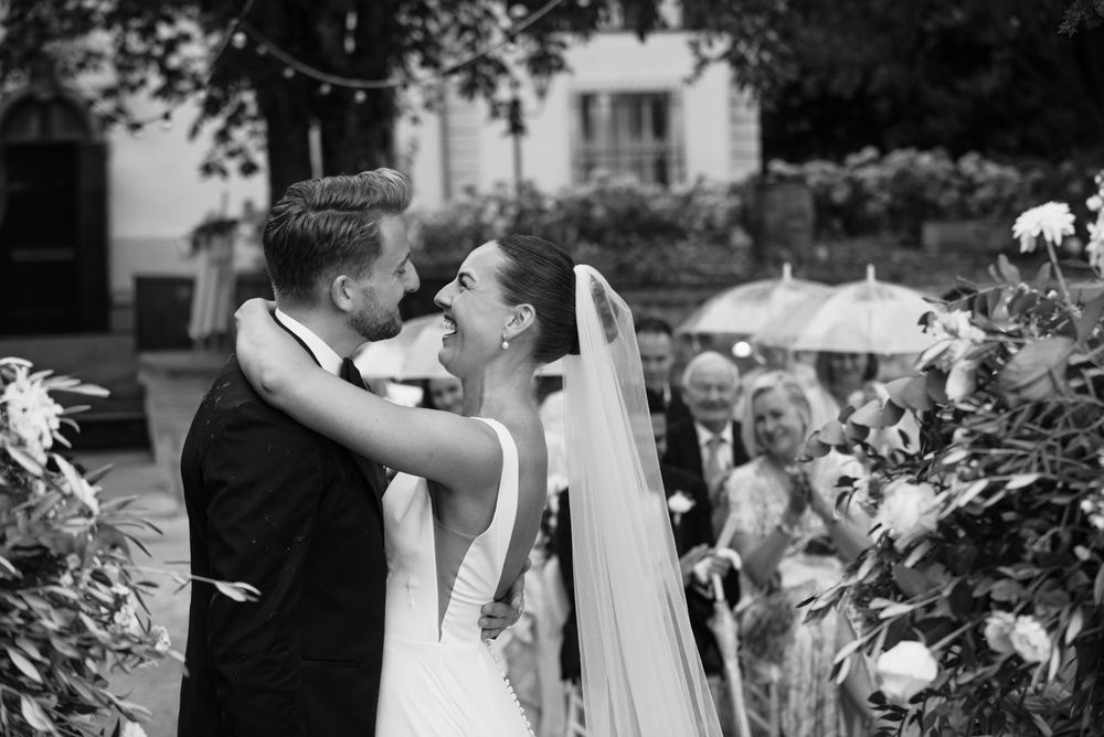 A romantic black and white wedding moment captured in a garden setting with guests in the background.
