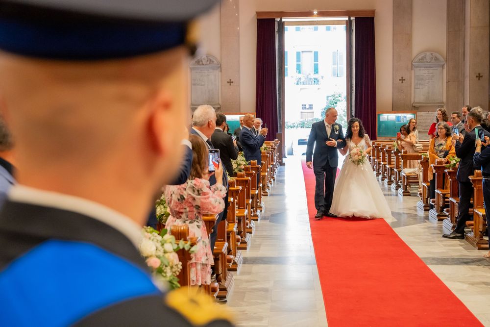 Guests seated in wooden chairs line both sides of a red carpet aisle runner during an indoor ceremony.