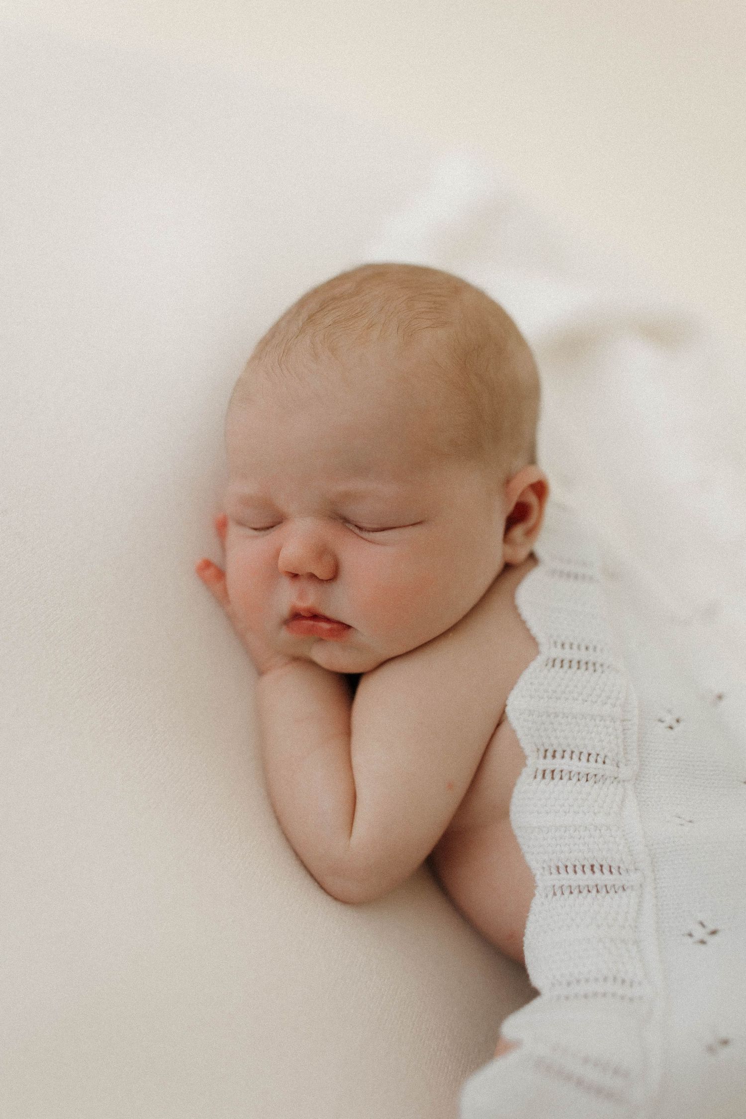 A sleeping newborn baby lies peacefully on white bedding while wrapped in a soft swaddle blanket.