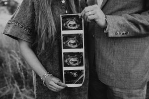 Couple holding ultrasound scan strip together outdoors, black and white maternity announcement photo.