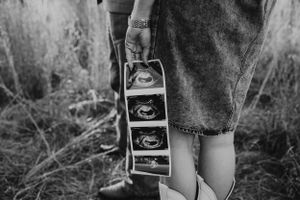 Couple holding ultrasound photos outdoors in a field, black and white pregnancy announcement photo.