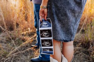 Expectant couple displaying ultrasound strip photos in a natural outdoor setting, color maternity announcement.