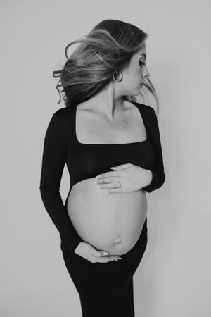 Pregnant woman in black dress cradling baby bump with flowing hair, elegant black and white maternity photo.