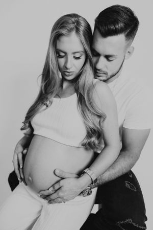 Black and white photo of a couple tenderly embracing, with the man holding the pregnant woman's baby bump.