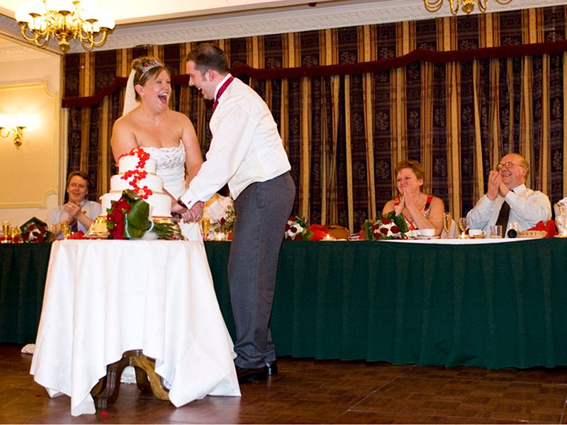 A newly married couple joyfully cutting their wedding cake, captured by High Wycombe photographer Abigail's Studio.