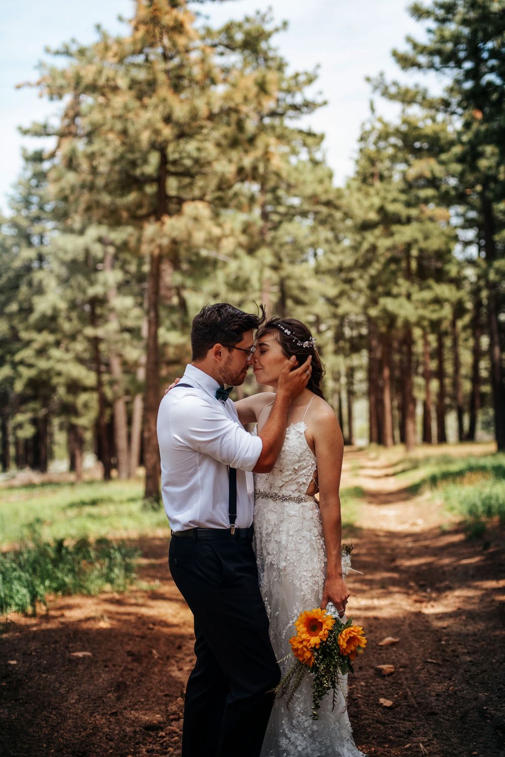 Wedding couple kissing, bride holding sunflowers at Lake Tahoe ceremony. Golden-hour glow through pine trees.