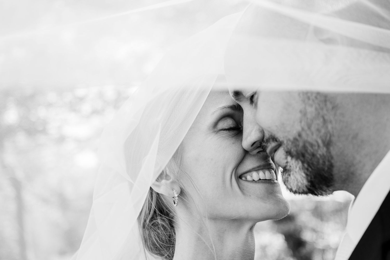 A black and white photograph of newlyweds standing on a rustic wooden bridge in a forest.
