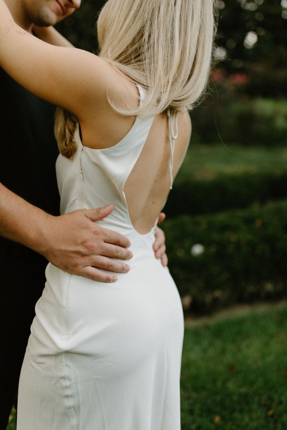 Intimate couple embraces in white dress against dark outdoor backdrop, showing romantic connection.