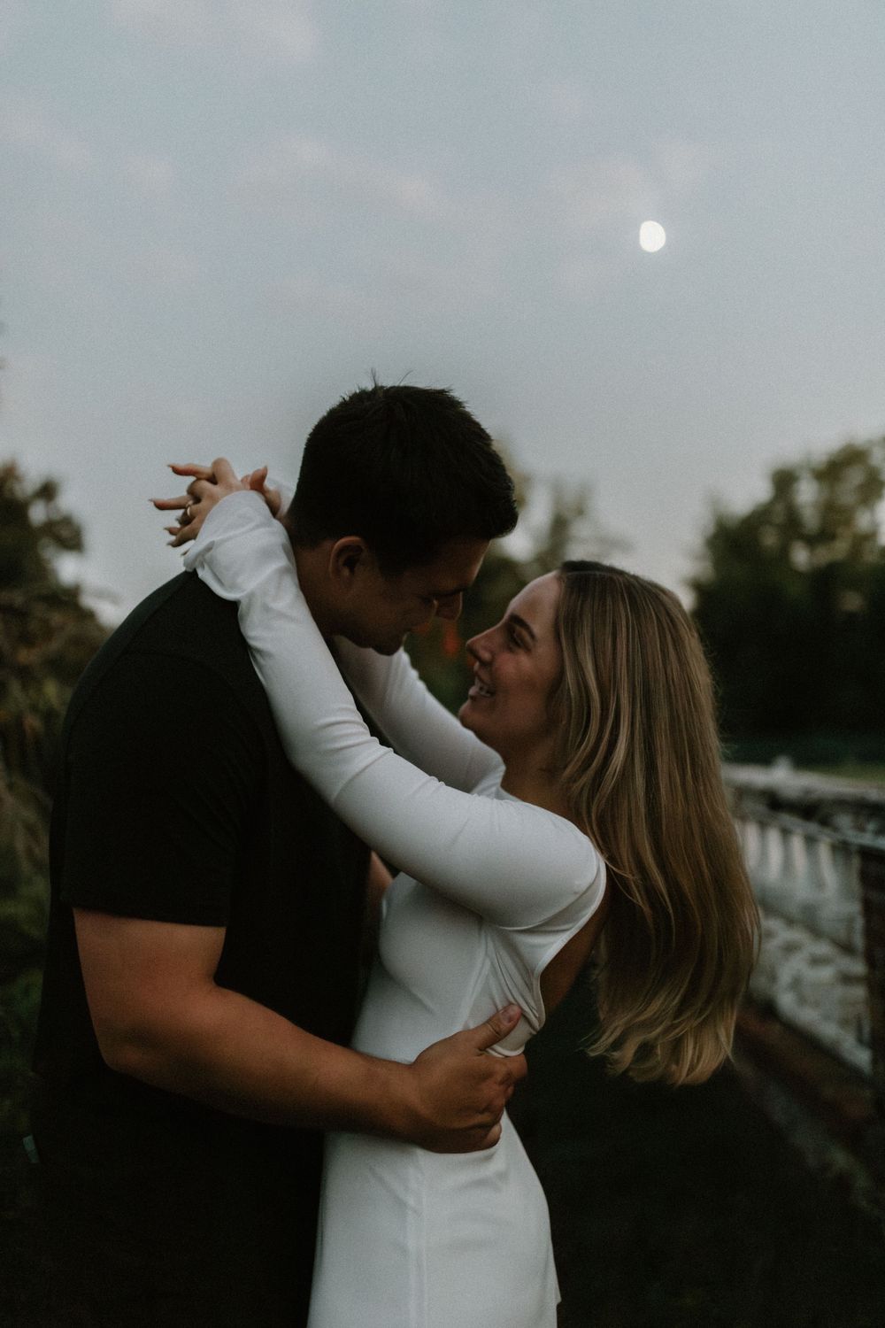 A romantic couple embraces and shares intimate moments at sunset against a moody sky.