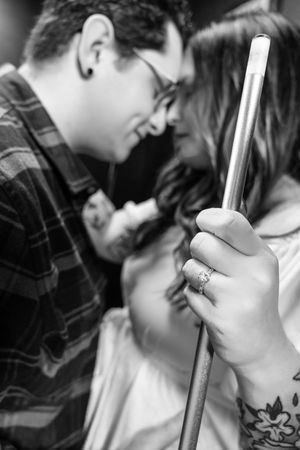 Black and white photo of a couple sharing a romantic moment, woman holding a pool cue with an engagement ring visible.