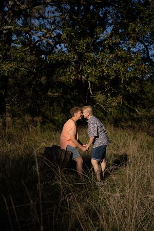 Two people sharing an intimate moment holding hands in a sunlit natural outdoor setting surrounded by tall grass and trees.