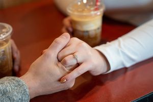 Couple holding hands on a table with iced coffee drinks, woman wearing a gold engagement ring.