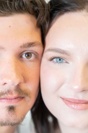 Close-up portrait of a young couple with brown and blue eyes, cheek to cheek, showcasing natural beauty.